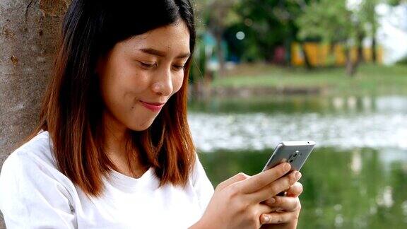 一名年轻的亚洲女子坐在公园里玩智能手机
