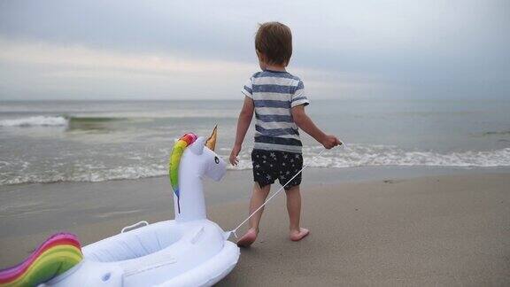 快乐的小男孩带着独角兽充气环在沙滩上奔跑