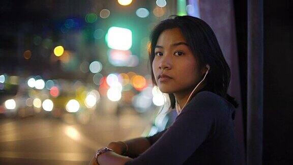 亚洲女人听音乐通过耳机在夜晚的城市