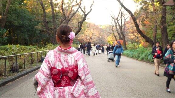 快乐年轻美丽的亚洲女人女孩穿着粉红色的传统日本和服走在公园的街道上看着远离东京城市日本的4K后视图