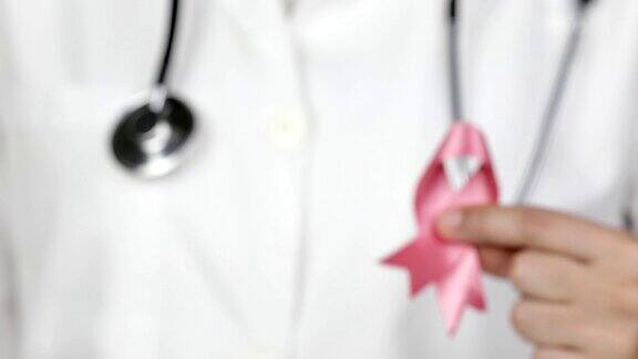 医生向镜头展示一条粉红色的乳腺癌意识丝带