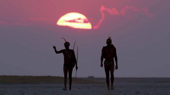 博茨瓦纳两名圣布须曼人正穿过Makgadikgadipan身后是夕阳西下的红色天空