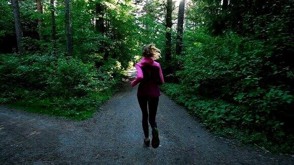 年轻的女孩在森林里奔跑一个女人在夏天的公园里慢跑慢镜头