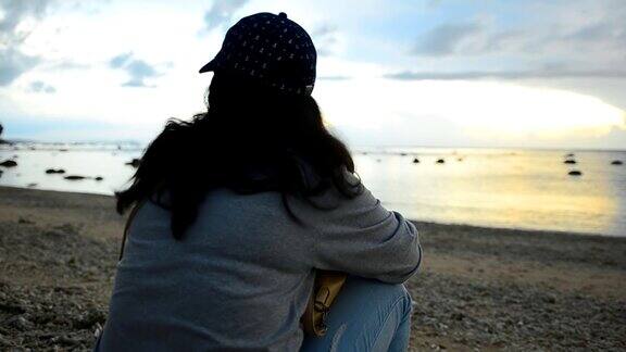 日落时分坐在海滩上的悲伤悲伤的年轻女子