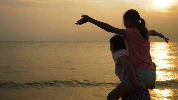 女孩背着她的母亲在海滩上日出的背景生活方式