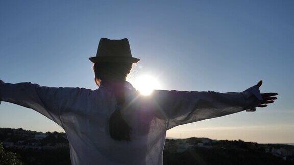 黎明时分一个女人站在山顶向太阳举起双手看着这座城市