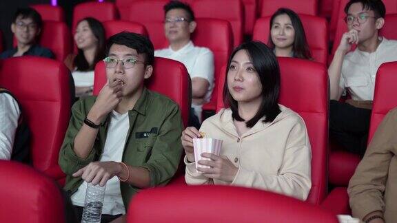 亚洲的中国年轻夫妇在电影院等待电影放映时分享食物享受彼此的陪伴