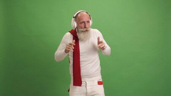 一位看起来像圣诞老人的老人用智能手机听音乐、跳舞、唱歌在绿色的背景上一个人