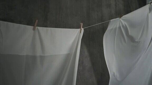 白色织物床单在绳子上的晒衣夹上晾干波浪状的织物在风中摇摆抽象的灰色背景