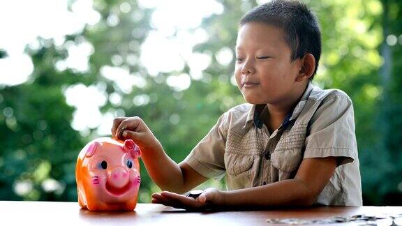 亚洲男孩带着快乐的微笑把硬币放入储蓄罐慢镜头散景背景存钱为将来攒钱