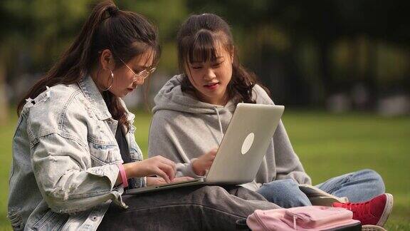 两个亚洲女大学生在校园里用笔记本电脑