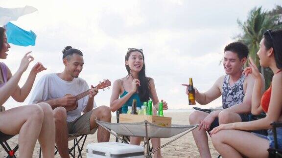 一群亚洲年轻男女在海滩上聚会迷人的快乐的朋友旅行者唱歌和跳舞在海边露营享受假期在热带海岛度假旅行