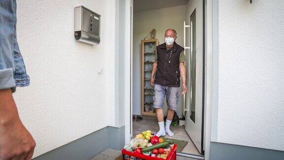 一名年轻女子在冠状病毒隔离期间将食品杂货送到一名老年男子的前门