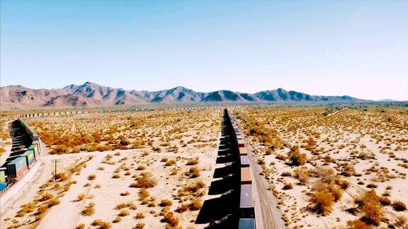 无人机从左到右跟踪一列集装箱货运列车这列火车在干旱的美国沙漠的铁路上飞驰而下
