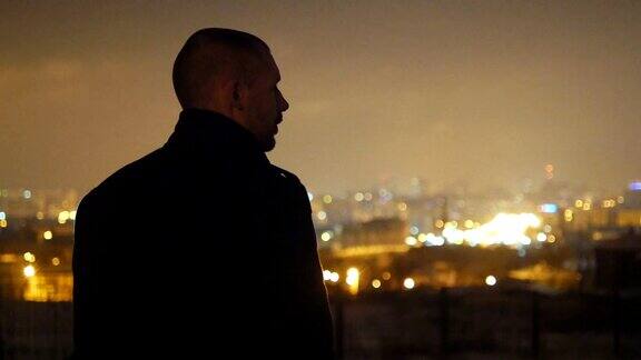 一个穿着夹克的年轻人站在外面抽着烟一个人看着他面前的城市夜景