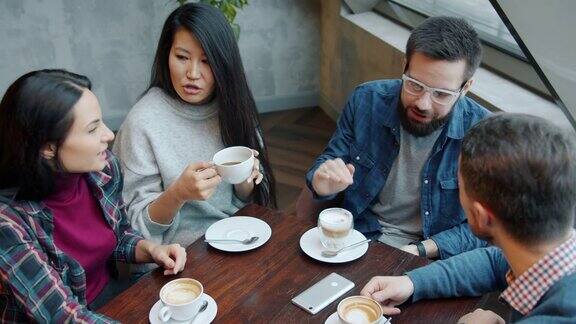 快乐的年轻女孩和男孩聊天和喝咖啡在咖啡馆的桌子上