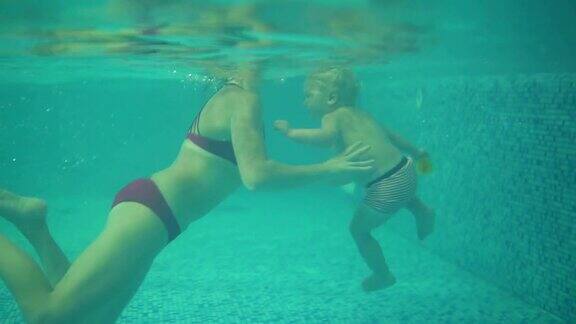可爱的金发小孩在游泳池的水下游泳他的妈妈正把他抬起来他妈妈正在教他游泳一个水下拍摄