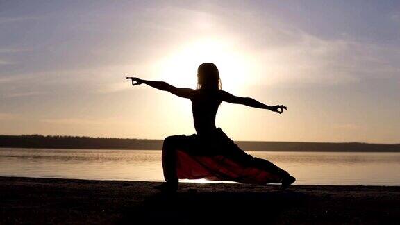 一个苗条女孩的剪影做武士合十礼瑜伽姿势在日落海边