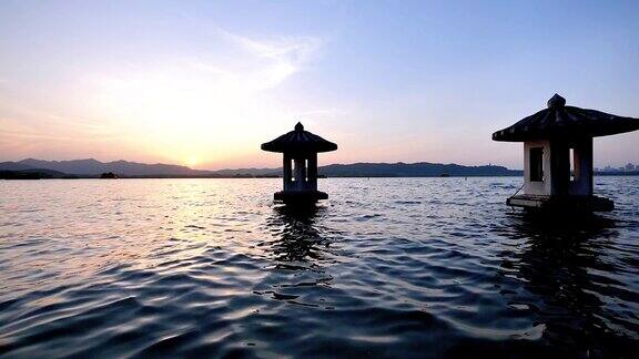 美丽的日落风景在西湖中国杭州橘色的黄昏天空和宁静的水与传统的亭台楼阁在湖中闪烁的涟漪超级慢的动作