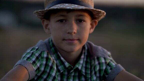 一个戴着草帽的乡村男孩在日落时看着摄像机的肖像