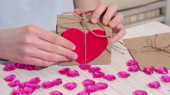 女性手在桌子上用红纸心装饰工艺礼盒用粉红色的心和礼物合起来情人节礼品包装情人节快乐