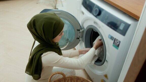 快乐的年轻穆斯林妇女戴着头巾在家洗衣服