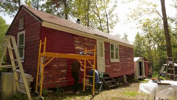时间的推移人们在一个农场粉刷一个小木屋红色
