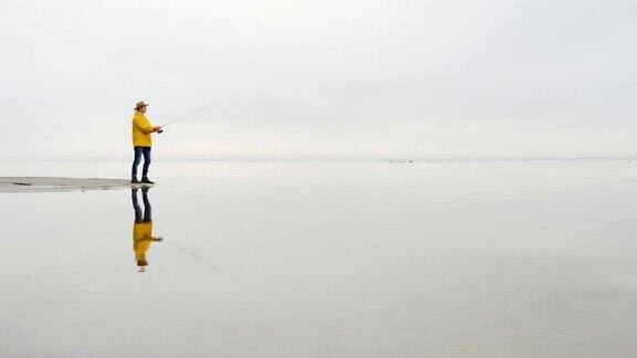 身穿黄色雨衣的渔民用慢动作抛出带有旋转杆的渔具