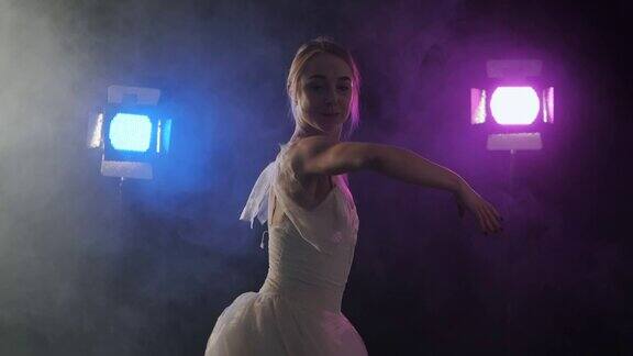 性感芭蕾舞女演员身穿古典或现代芭蕾舞元素的白色芭蕾舞裙在黑暗中旋转泛光灯背景下有蓝色和紫色的光和烟雾