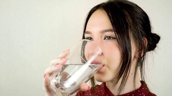 一个年轻的女人从一个透明的玻璃杯里喝水特写镜头