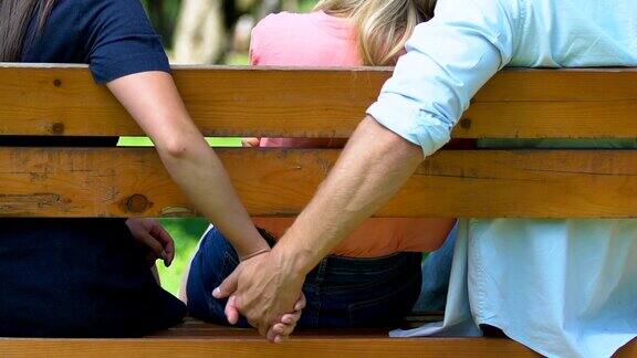 年轻男子在长椅上抚摸女友的手靠近女友的背叛