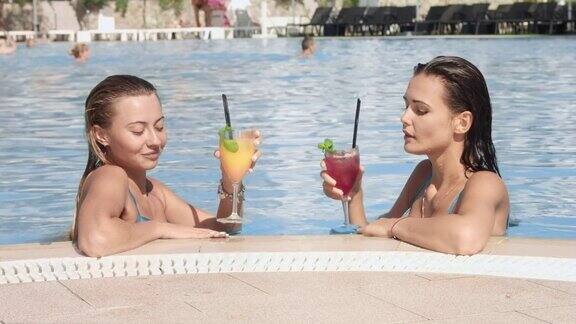 两个女孩在泳池边喝着鸡尾酒在泳池里游泳