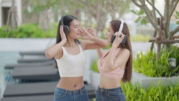 美丽的亚洲女性戴着耳机听着音乐在豪华酒店的游泳池边聚会边唱歌跳舞放松身心享受休闲活动生活方式在假期