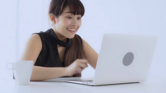 美丽肖像自由职业的年轻亚洲女人微笑和愉快的工作在线笔记本电脑成功与兴奋在客厅在办公室女孩自信使用笔记本商业和沟通