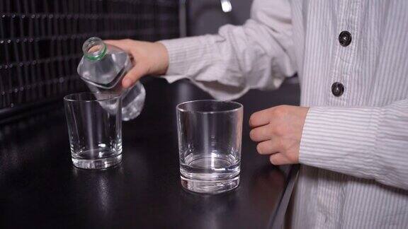 一个女人的手拿起一个塑料瓶把水倒进玻璃杯里
