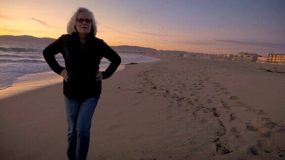 活跃迷人的成熟女人走在日落的海滩上