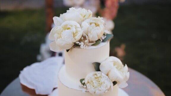 用白色牡丹花装饰的婚礼蛋糕特写慢动作美丽的婚礼蛋糕白色婚礼拱门的背景