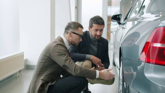 男人客户和推销员在展示厅谈论汽车看轮胎的慢动作
