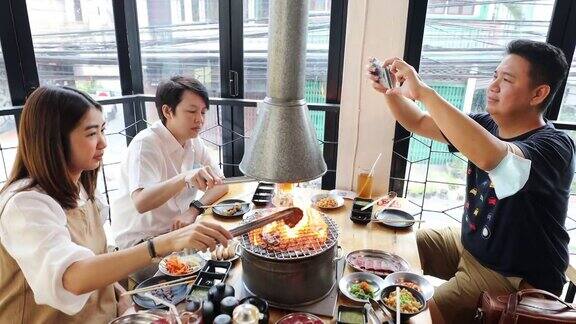 亚洲成年朋友在烧烤餐厅用智能手机拍照和录像