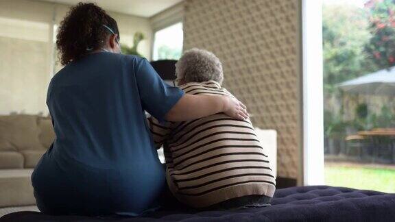 家庭护理人员帮助一位老年妇女站在家里-医生戴着防护口罩