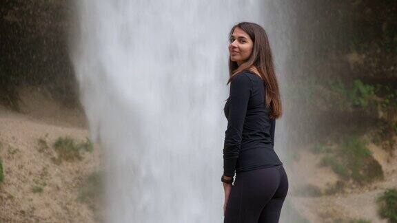 年轻女子站在瀑布前微笑着回头看