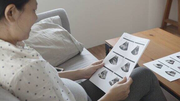 亚洲孕妇坐在沙发上看超声波图像