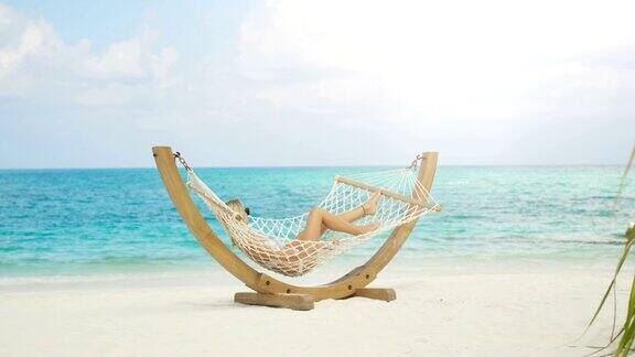 田园诗般的场景美丽的女人日光浴躺在吊床上的海滩蔚蓝的海滩白沙和海蓝宝石的水阳光普照异国风情