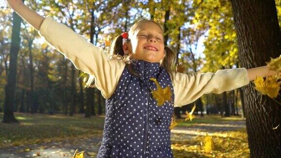 一个小女孩在秋天的公园里跳着扔着黄叶