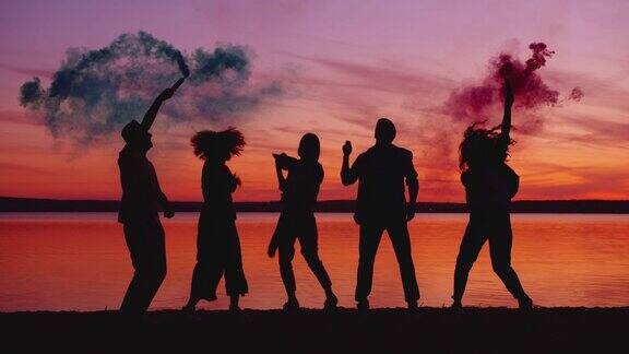 人们在日落时在海滩上跳舞拿着烟雾弹享受户外聚会
