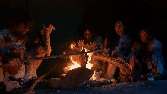尼安德特人或智人家庭在篝火上烹饪动物肉然后吃它史前狩猎采集者部落穿着兽皮晚上在黑暗可怕的洞穴里吃东西