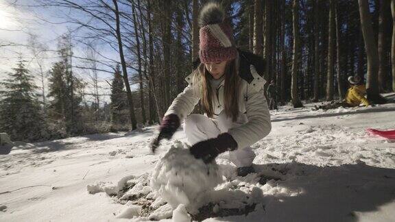 在一个阳光明媚的冬日一个十几岁的女孩正在森林里堆雪人
