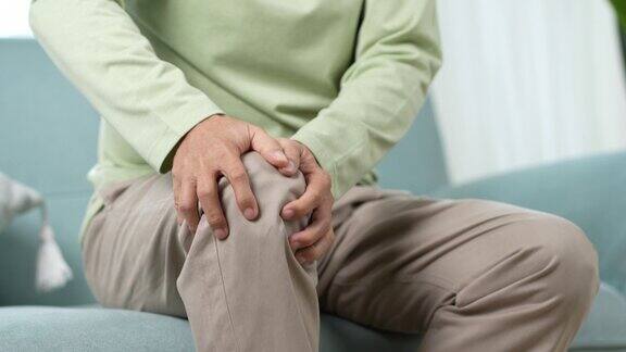 亚洲高级男子感到膝盖疼痛疼痛年长的成年男性坐在家里客厅沙发上时膝盖受伤骨骼问题保健与医疗保险概念