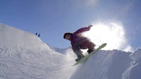 慢动作:年轻的专业滑雪板运动员在阳光灿烂的雪园的半管喷洒雪