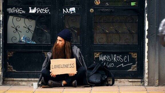 无家可归的人拿着“孤独”纸板在拥挤的街道上乞讨